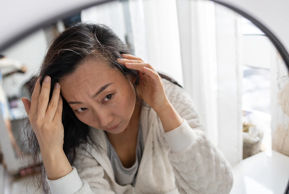 鏡を見ながら、髪の生え際や白髪を確認する女性。