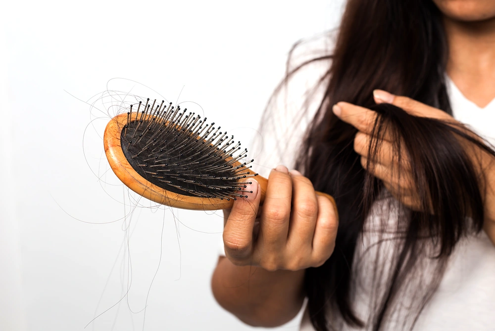 ヘアブラシに絡まった抜け毛を確認している女性。