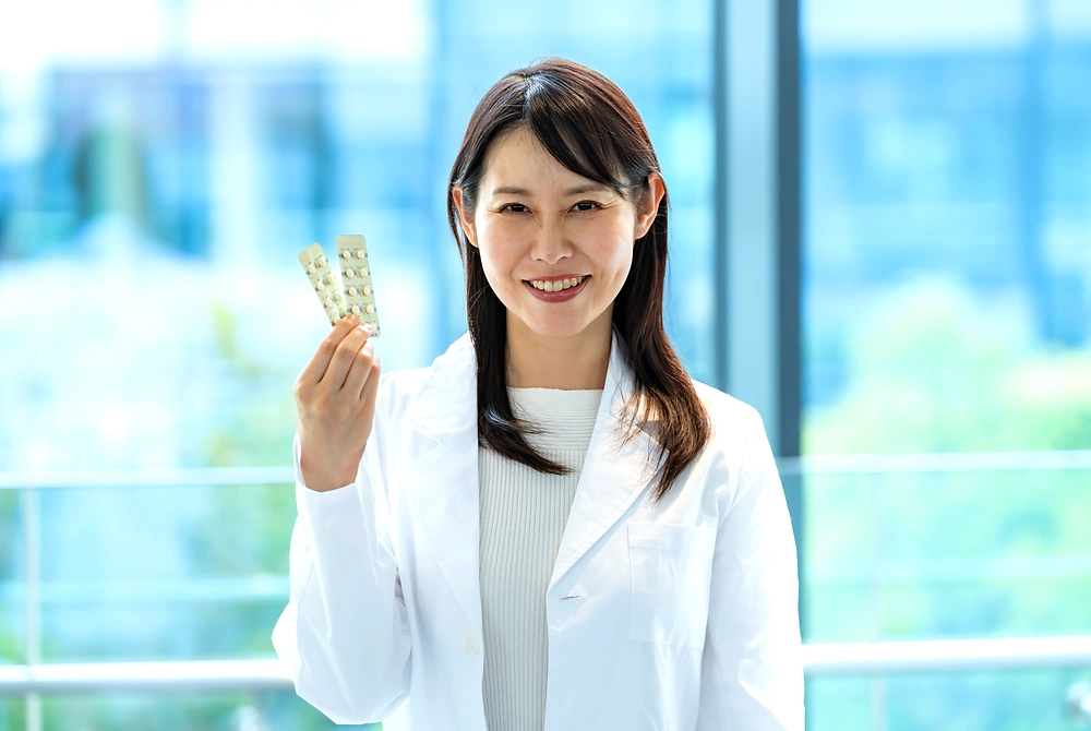 白衣を着た女性が、薬のシートを手に持って説明している様子。