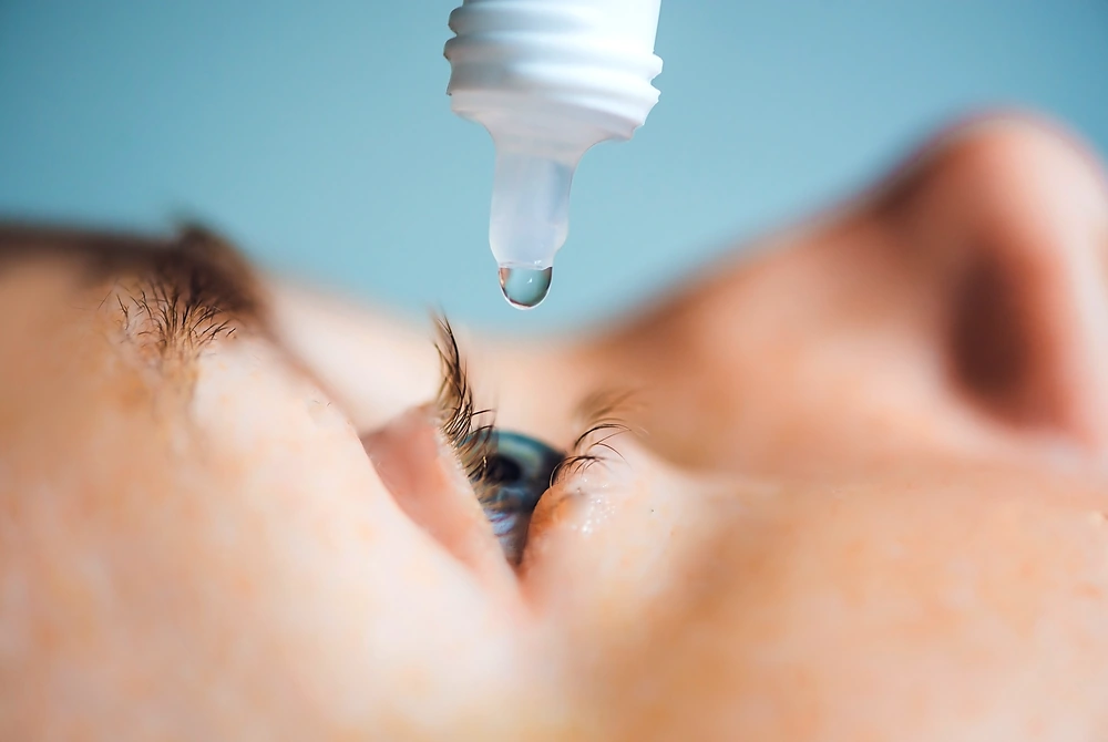 横になった人の目に、点眼薬をさそうとしている様子。