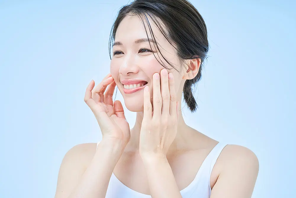 頬に手を添えて笑顔を見せる女性の美容イメージ。