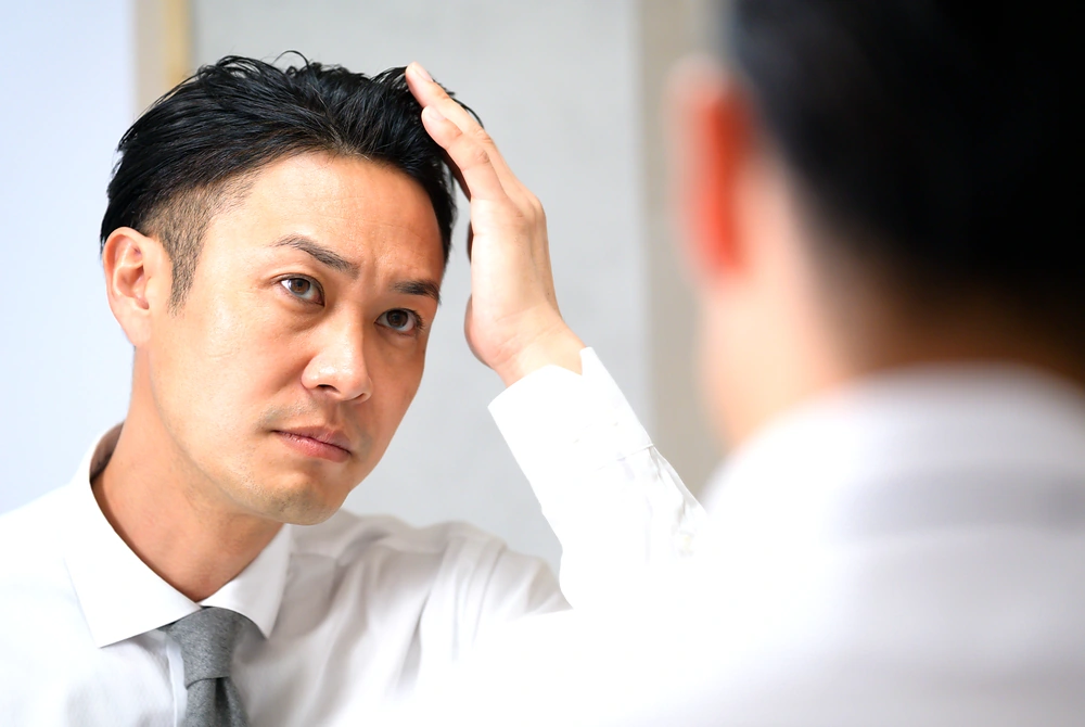 鏡の前で生え際や頭頂部の髪の状態を確認する男性。