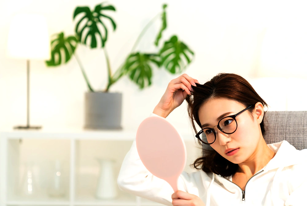 手鏡を持ち、髪の分け目や生え際を確認する女性。