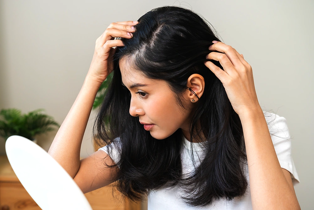 鏡の前で髪を左右に分け、頭皮や分け目の状態を確認する女性。