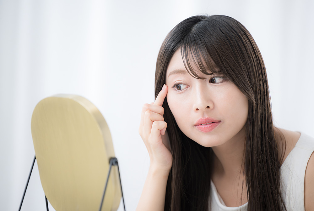 鏡を見ながら目元の肌の状態を確認する女性。