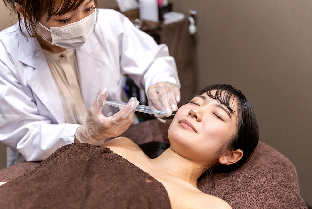 美容医療の施術室で、女性が頬への注入治療を受けている様子。