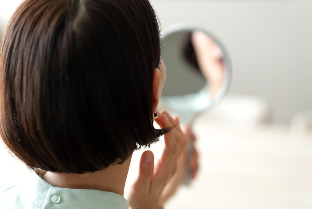 手鏡で顔を確認しながら、頬やあご周りの肌の状態を気にする女性。