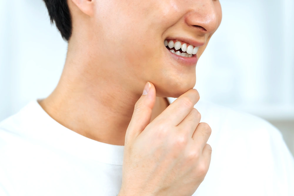 鏡を見ながら頬にスキンケアクリームを塗る男性。