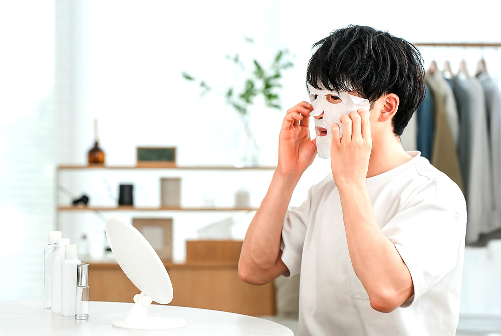 鏡の前でフェイスシートを顔にのせる男性。