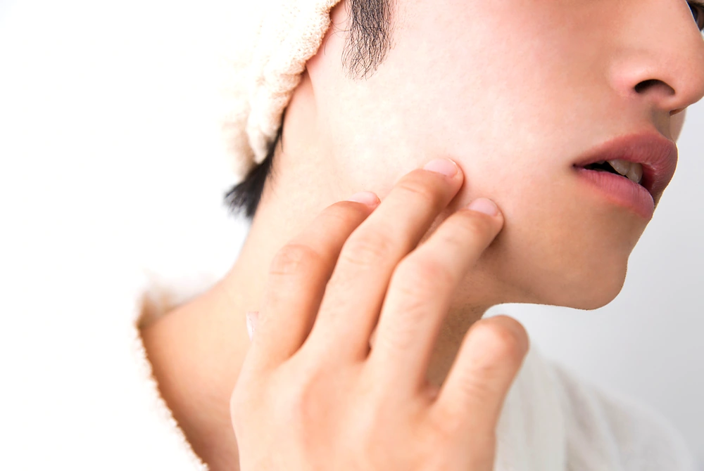 頬の肌に触れ、ニキビ痕や肌質を確認している男性の横顔。