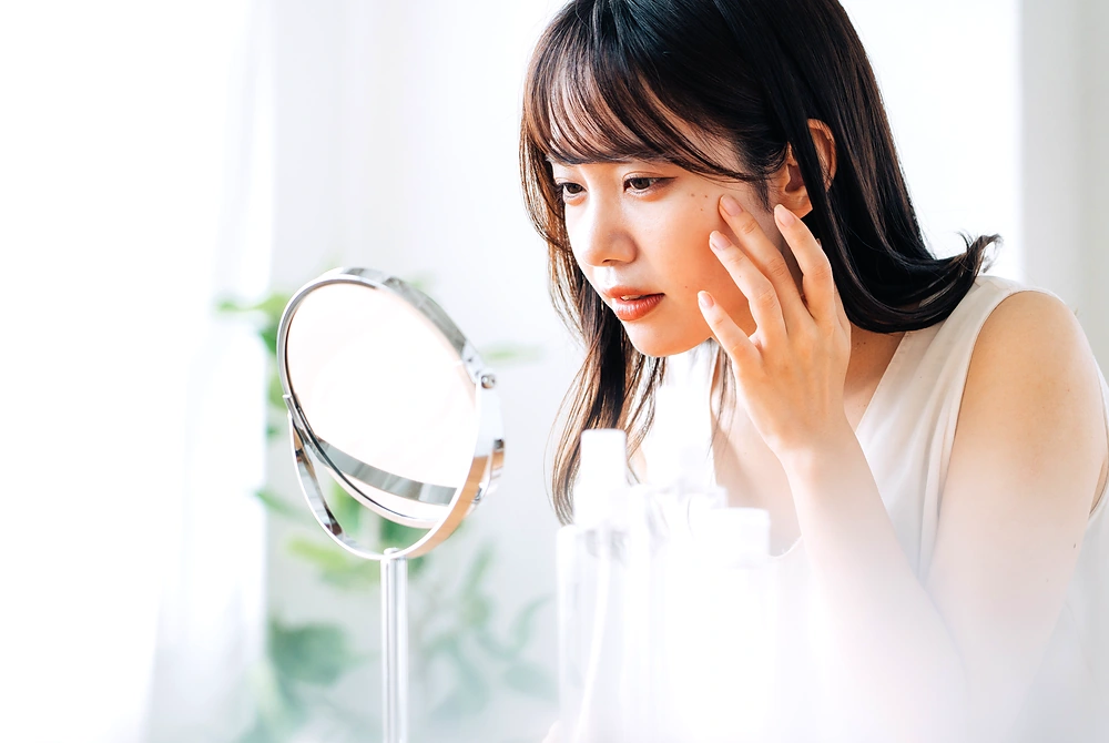 鏡を見ながら頬の肌状態を確認する女性。
