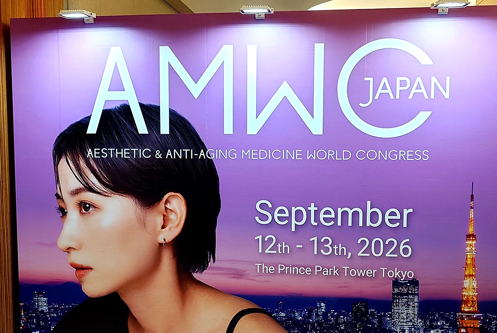 AMWC Japan 2026の開催日程と会場名が記された、東京の夜景を背景にした会場パネル。