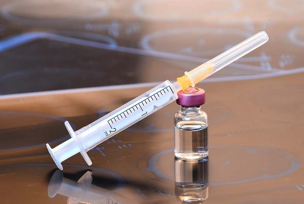 薬剤バイアルの上に注射器が置かれた、美容注射を連想させるイメージ。