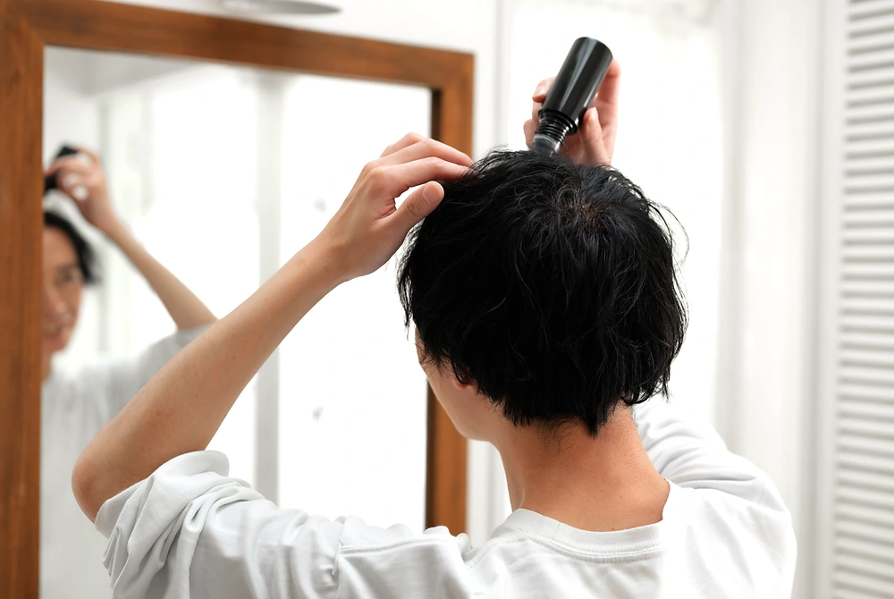 男性が鏡の前で頭皮に外用剤を塗布している様子。