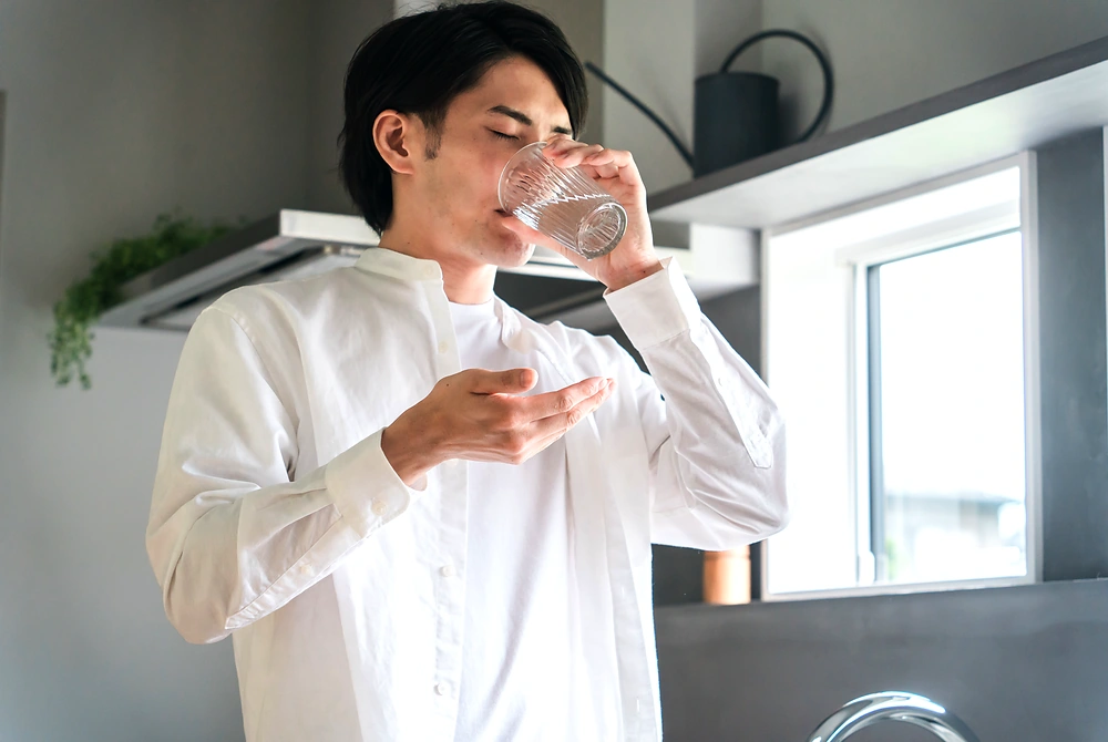 男性がコップの水で錠剤を飲んでいる様子。