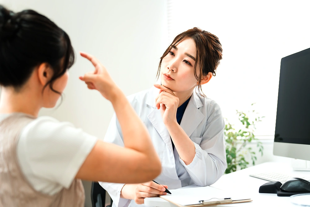 美容医療の診察室で、医師が患者の顔の悩みを聞きながら相談している様子。