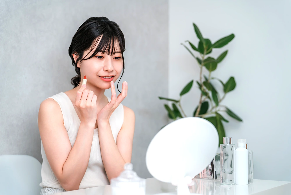 鏡の前でリップケアをしながら、肌や顔全体の印象を確認する女性。