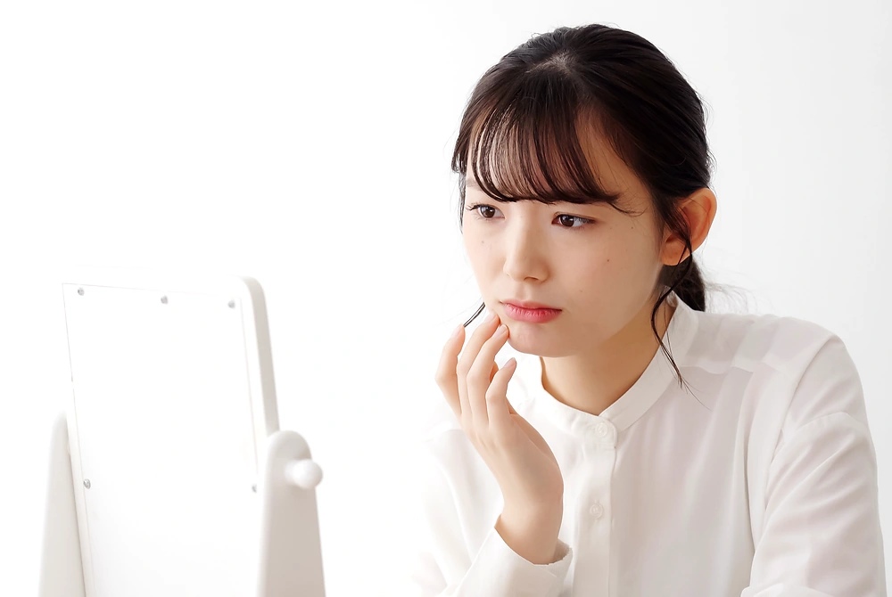 卓上ミラーを見ながら、頬や口元の肌の状態を気にする女性。