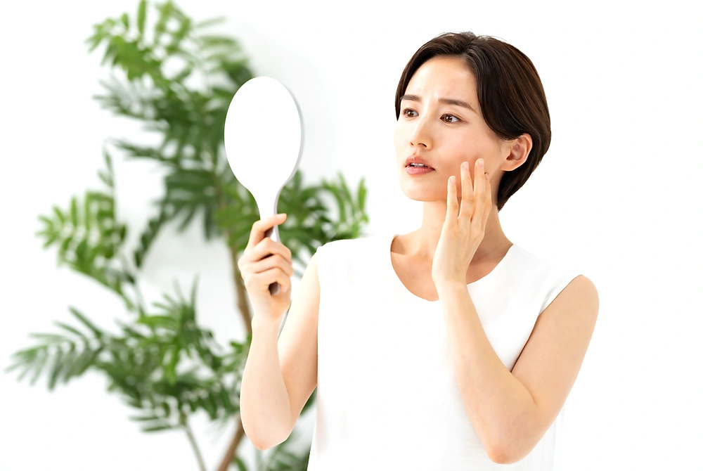 鏡を見ながら頬に手を当て、肌の状態を確認する女性。