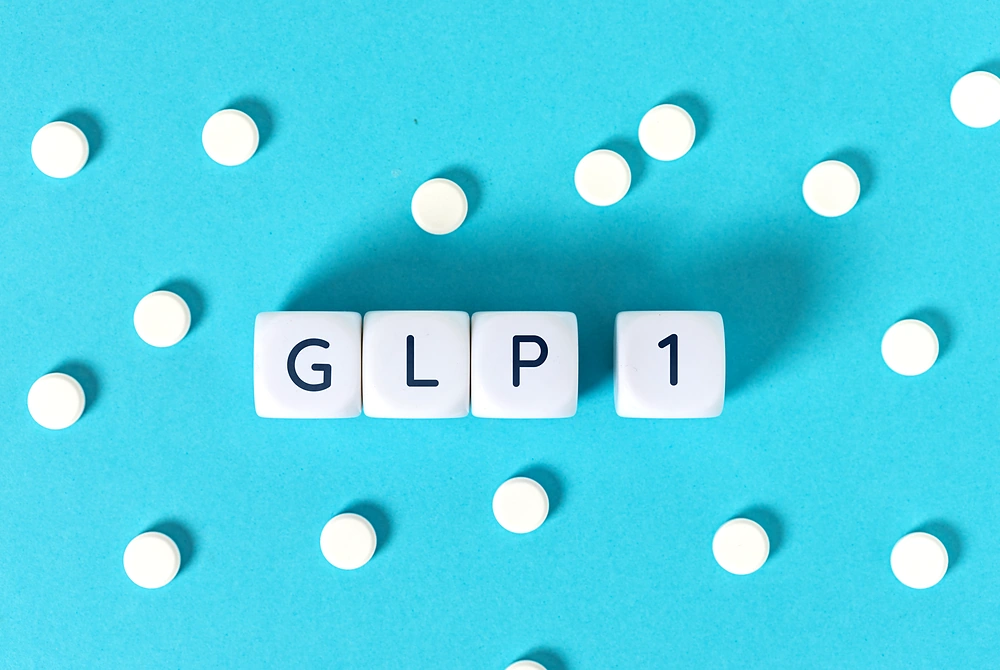 青い背景の上に「GLP 1」と書かれたブロックと白い錠剤が置かれている。