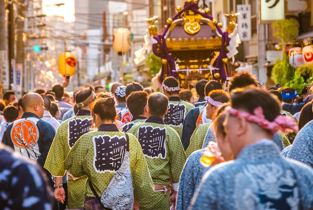 祭りの法被を着た人々が、神輿を担いで街を進む様子。