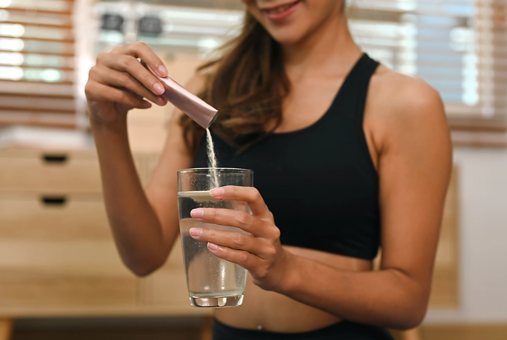 運動着の女性が、スティック状の粉末を水の入ったグラスに入れている。