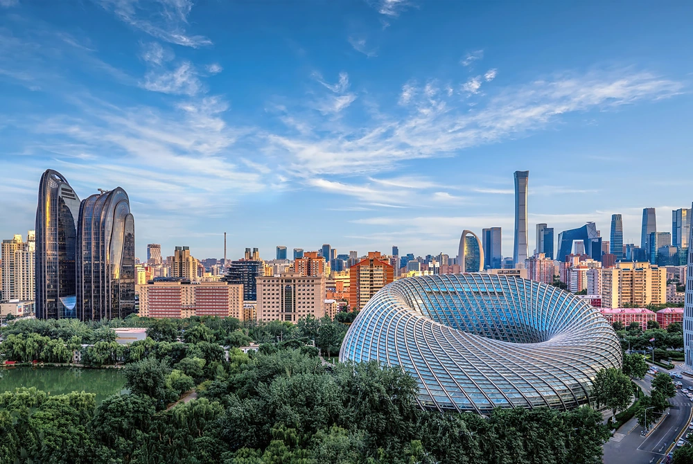 中国・北京市の都市景観。特徴的な曲線を描くガラス張りの建築物を中心に、高層ビル群と緑豊かな公園が広がっている。